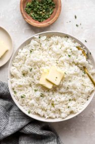 A bowl of cooked white rice topped with two pads of butter.