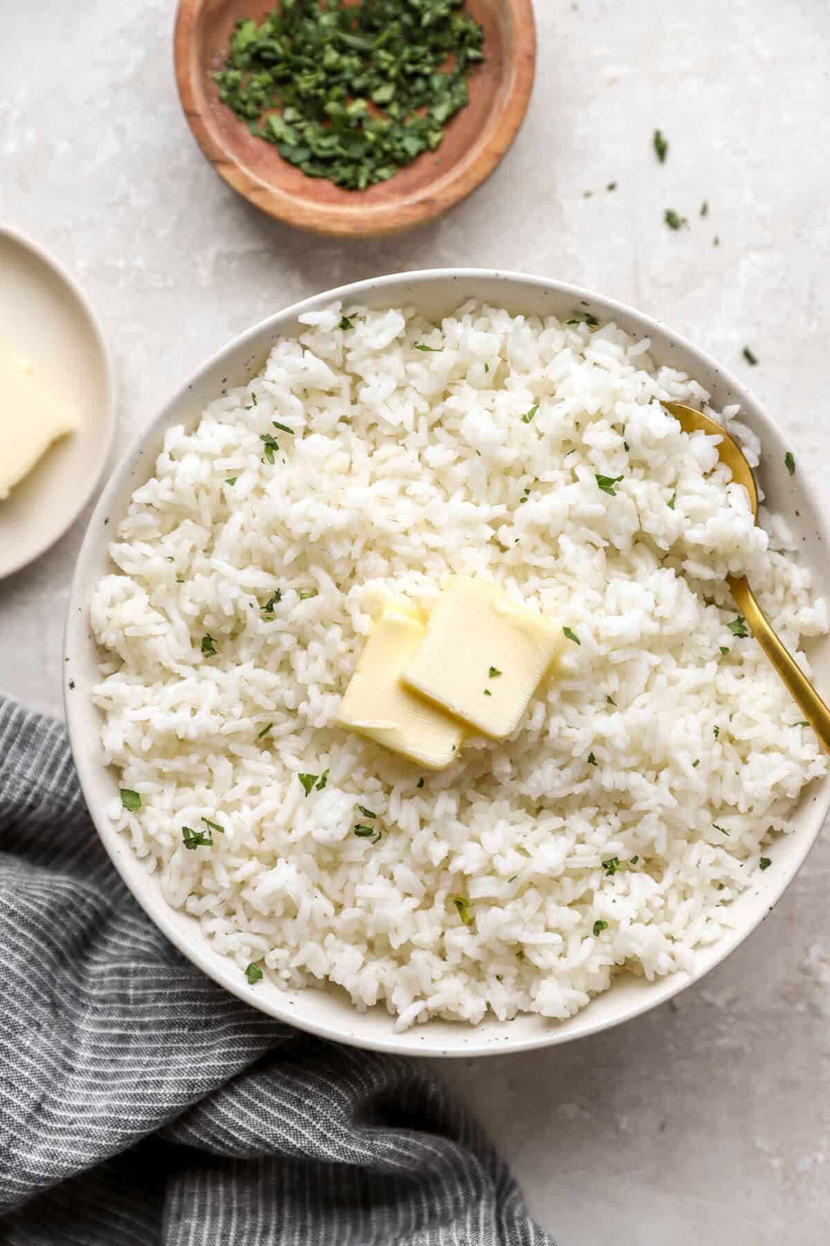 A bowl of cooked white rice topped with two pads of butter.